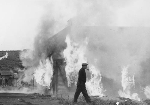 Photo of man walking past burning building.