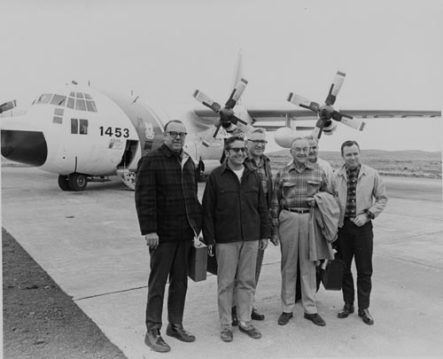 Photo of six men standing in front of a airplane.