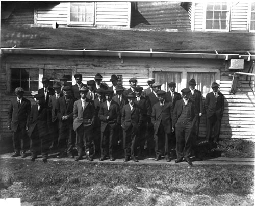Photo of a group of native men and boys in suits and hats.