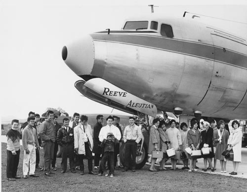Photo of young men and women standing in front of an airplane.