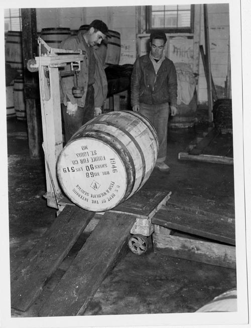Photo of two men weighing a barrel of the Fouke Fur company.
