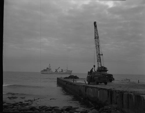 Photo of crane on shore with ship "Penguin" in the background.