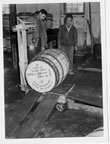 Thumbnail photo of two men weighing a barrel of the Fouke Fur company.