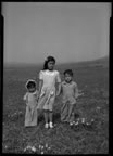 Thumbnail photo of three children standing in flower strewn field.