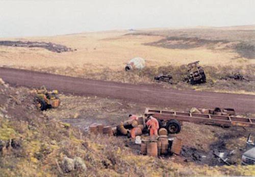 Photo of piles of rusted oil drums alongside a dirt road at the Oil Drum Dump Site.