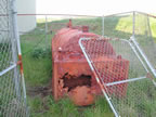 Thumbnail photo of a rusty machine behind a half-collapsed chain link fence, the School AST.