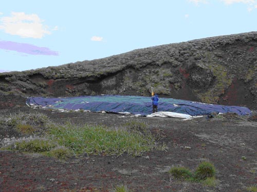 Photo of a person standing near blue tarp on hillside surveying the soil stockpile at Polovina Hill using Global Positioning System.
