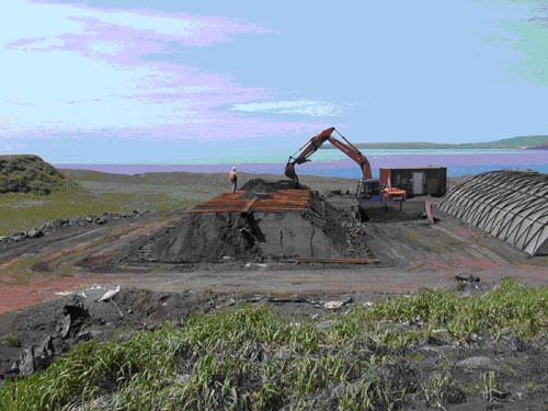 Photo of construction of an Enhanced Thermal Conduction treatment cell at the Blubber Dump showing a partially completed low structure with a person standing on top and an excavator in the background.