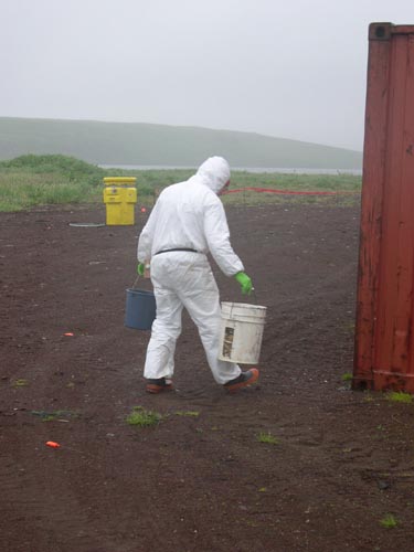 Photo of NOAA staff in white protective gear carrying two buckets removing asbestos fragments from NOAA Tract 50.