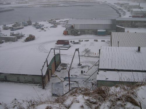 Photo of view of the Tract 46 Sheet Metal Garage after demolition showing an empty space between snow covered buildings.