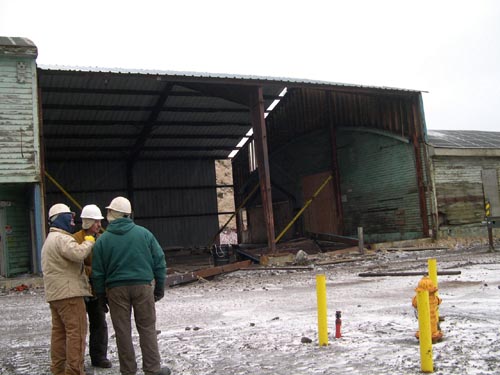Photo of three people standing near the half-demolished Tract 46 Sheet Metal Garage.