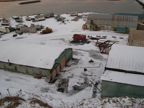 Photo of view of the Tract 46 Sheet Metal Garage from Village Hill after demolition showing snow covered buildings, equipment, and boats.