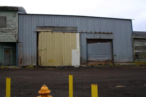 Photo of the Tract 46 Sheet Metal Garage prior to demolition, a metal-sided blue building.