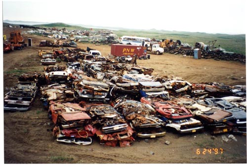 Photo of the vehicle Boneyard site prior to remediation showing stacks of crushed cars and other vehicles.