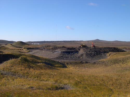 Photo of view of the petroleum contaminated soil stockpile in Cell C of the St. Paul Landfill showing an expanse of dry grass with heavy equipment on a dirt area in the background.