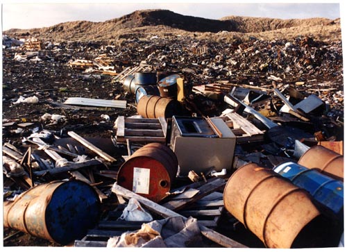 Photo of rusted barrels and other debris scattered in large piles.