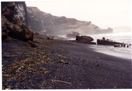 Photo of large pieces of rusted metal debris on rocky shore.