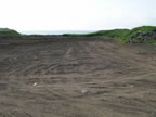 Thumbnail photo of an expanse of bare earth showing the petroleum contaminated soil stockpile location at the Blubber Dump after remediation.
