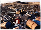 Thumbnail photo of rusted barrels and other debris scattered in large piles.