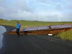 Thumbnail photo of person standing on shore near large rusted metal slab.