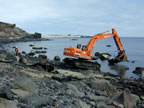 Photo of mechanical crane in water of rocky shore.