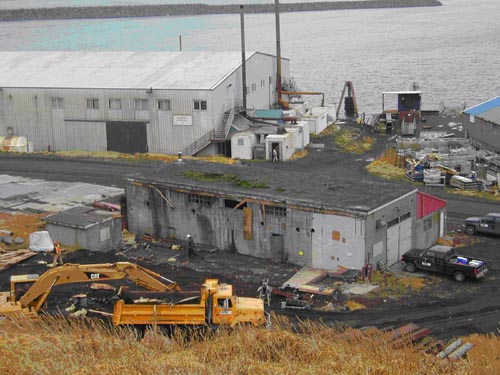 Photo of two buildings near water surrounded by construction material and equipment.