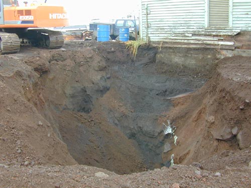 Photo of a hole in the ground at the base of a weathered blue building.