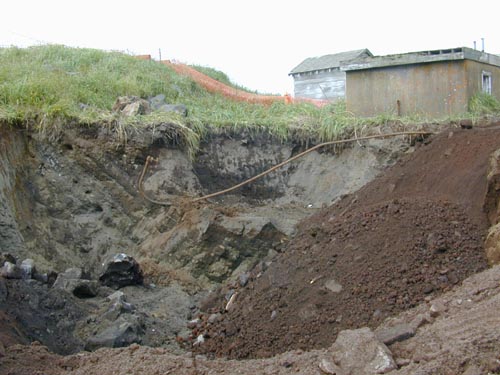 Photo of a large hole in the ground near two buildings.