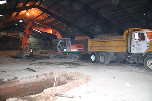 Photo of the interior of a large building with excavator digging a hole.