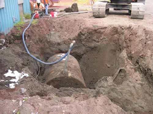 Photo of a large hole with large cylinder attached to long hose.