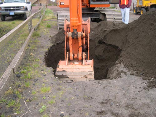 Photo of an excavator digging a hole near a wooden fence.