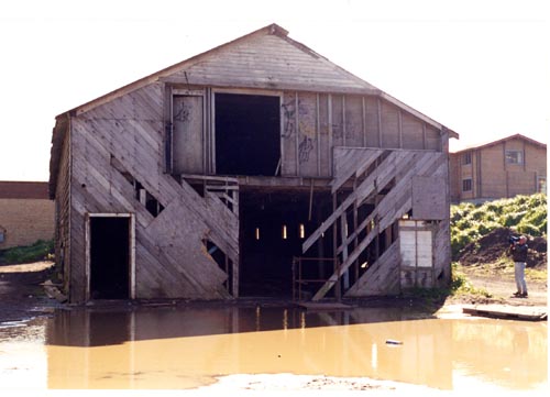 Photo of a  large, open building surrounded by a large pool of muddy water.