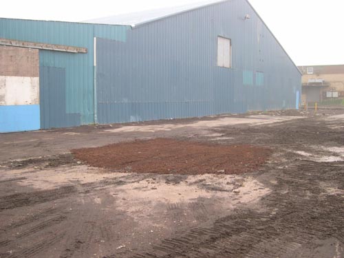 Photo of bare dirt area outside of a blue building.