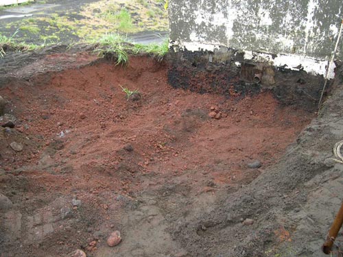 Photo of a shallow hole with red soil.
