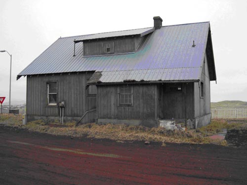 Photo of a gray building near a dirt road.