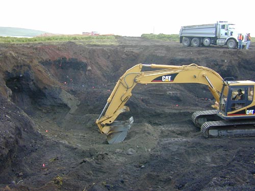 Photo of an excavator digging in a large hole.