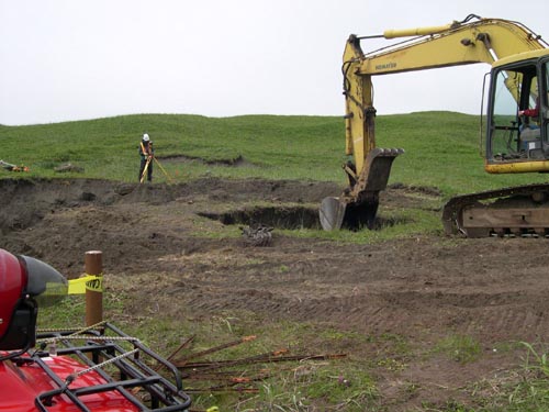 Photo of an excavator digging a hole in a grassy area.