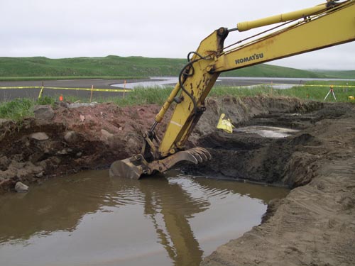Photo of an excavator digging in hole filled with water.