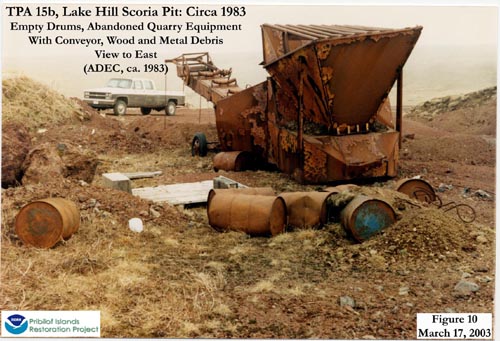 Photo of empty drums, abandoned quarry equipment with conveyors, and wood and metal debris at Lake Hill Scoria Pit.
