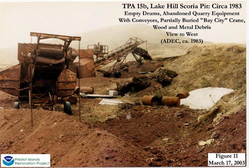 Photo of empty drums, abandoned quarry equipment with conveyors, partially buried "Bay City" crane, and wood and metal debris at Lake Hill Scoria Pit.