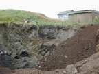 Thumbnail photo of large hole in the ground near two buildings.