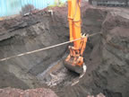 Thumbnail photo of an excavator digging a hole at the base of a blue building.