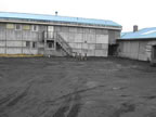 Thumbnail photo of a weathered gray building with a blue roof.