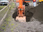 Thumbnail photo of an excavator digging a hole near a wooden fence.