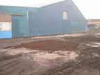Thumbnail photo of a bare dirt area outside of blue building.