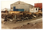 Thumbnail photo of rocks and wooden material outside of a large gray building.