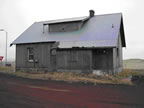 Thumbnail photo of a gray building near a dirt road.