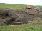Thumbnail photo of a large hole cordoned off with caution tape.