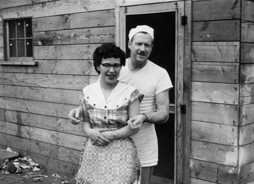 Photo of man and woman outside of wooden building.