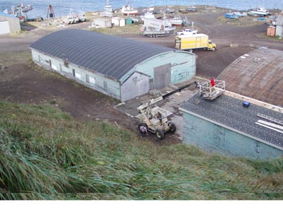 Photo of low blue building surrounded by small boats and heavy equipment.